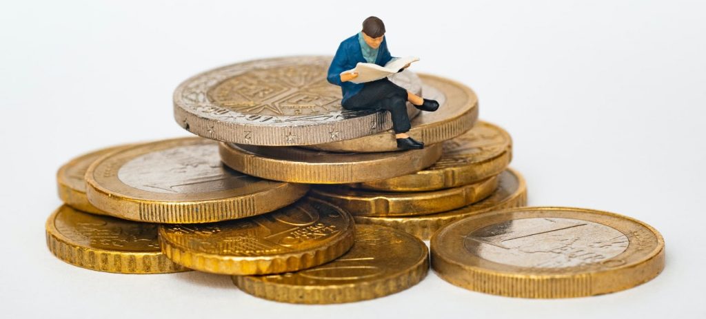 Boneco da miniatura de um homem sentado em cima de uma pilha de moedas