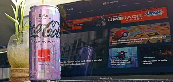 A latinha da Coca-Cola Byte sem açúcar, edição limitada criada no metaverso pela marca; ao fundo o site do TecMasters na tela de um notebook