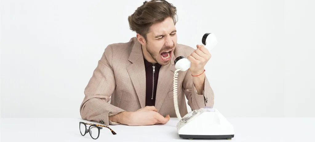 Na imagem aparece um homem jovem vestido com um terno e gritando em um telefone, representando as ligações indesejadas e chamadas de spam que podemos receber via telefone