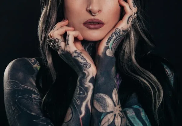 Imagem mostra uma mulher com cabelos longos escuros e mechas loiras, mostrando os braços adornados com tatuagem